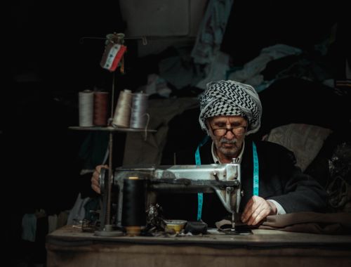Free An elderly tailor skillfully sewing in a traditional atelier in Iraq, surrounded by fabrics. Stock Photo