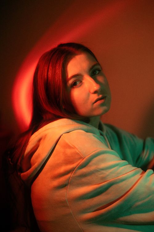 Free A captivating portrait of a woman in a hoodie illuminated by dramatic red and green lighting. Stock Photo