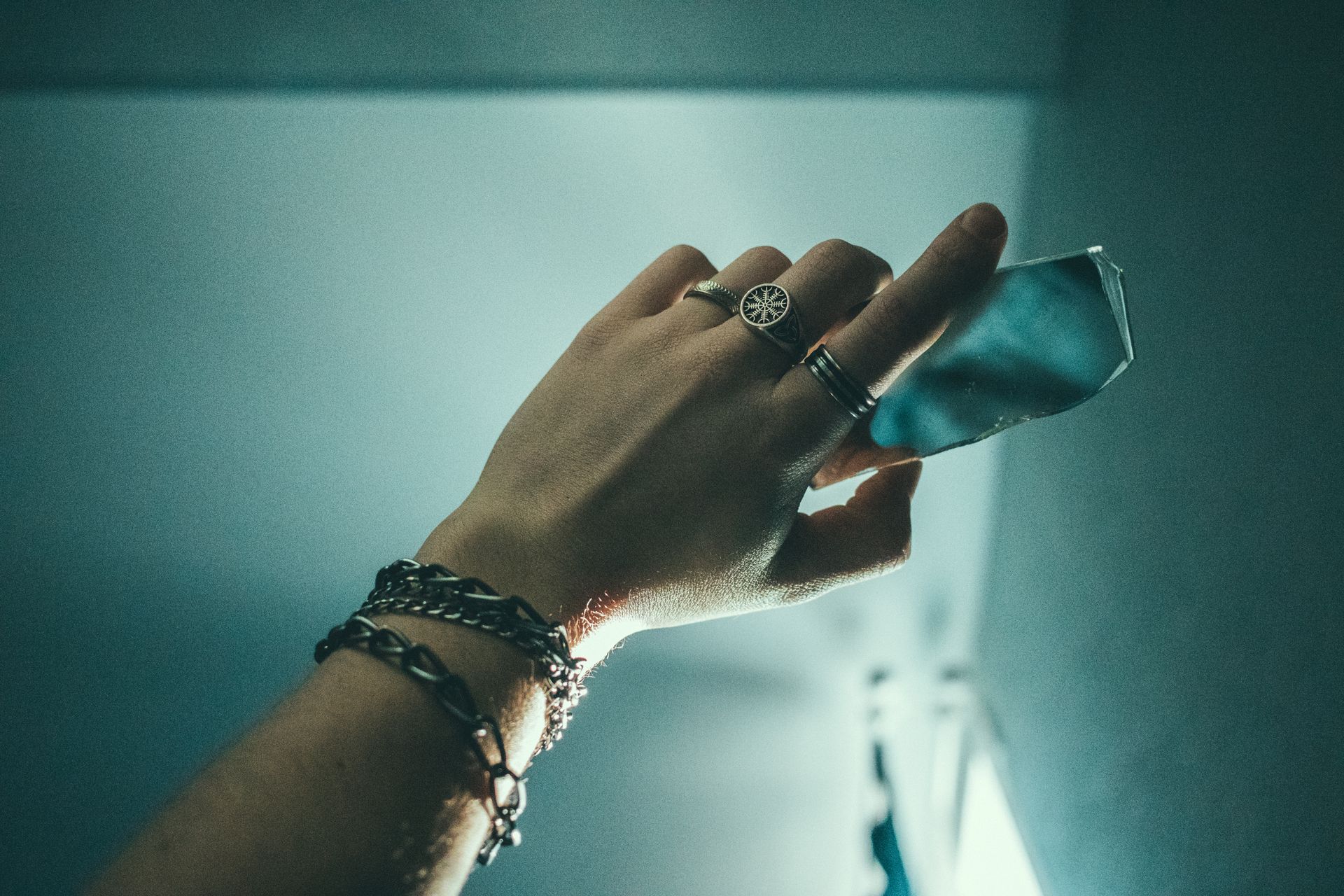 A hand adorned with silver jewelry holds a reflective glass piece against a stylish background.