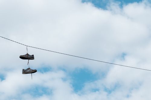 Free A pair of sneakers hanging on a wire with a background of a bright blue sky and white clouds. Stock Photo