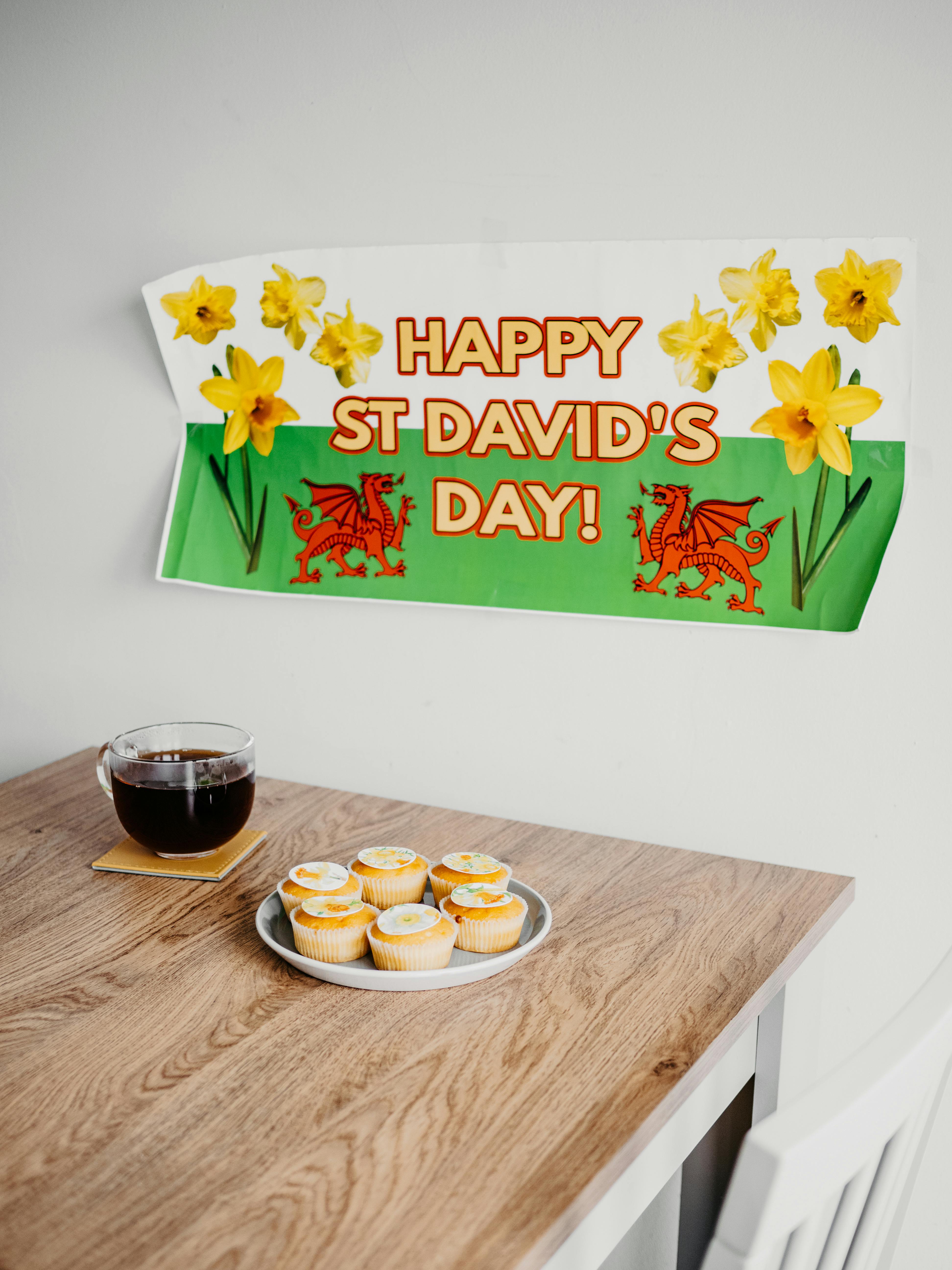 Festive St. David's Day setup featuring daffodils, cupcakes, and a tea cup on a wooden table.