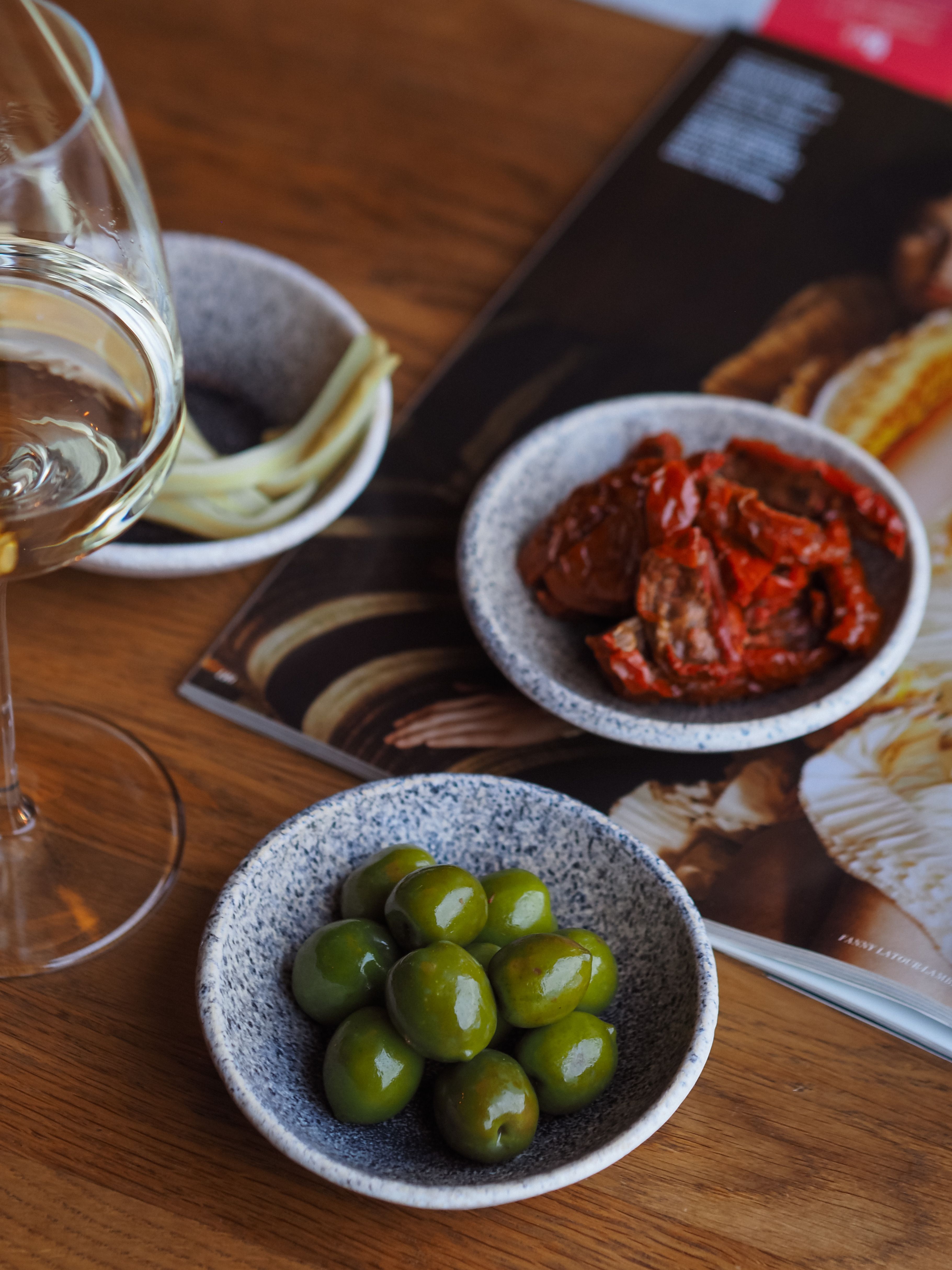 A gourmet spread featuring olives, dried tomatoes, and wine on a wooden table.