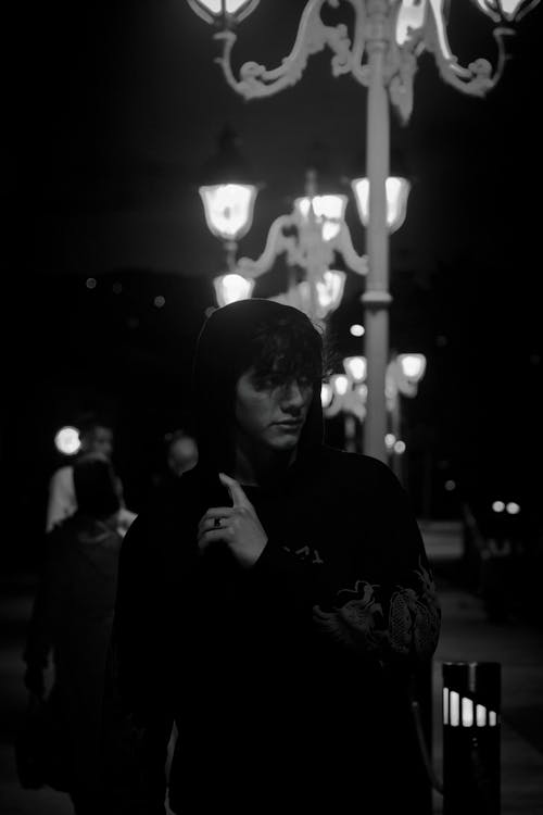 Grayscale Photo of Man Standing beside White Street Lamp
