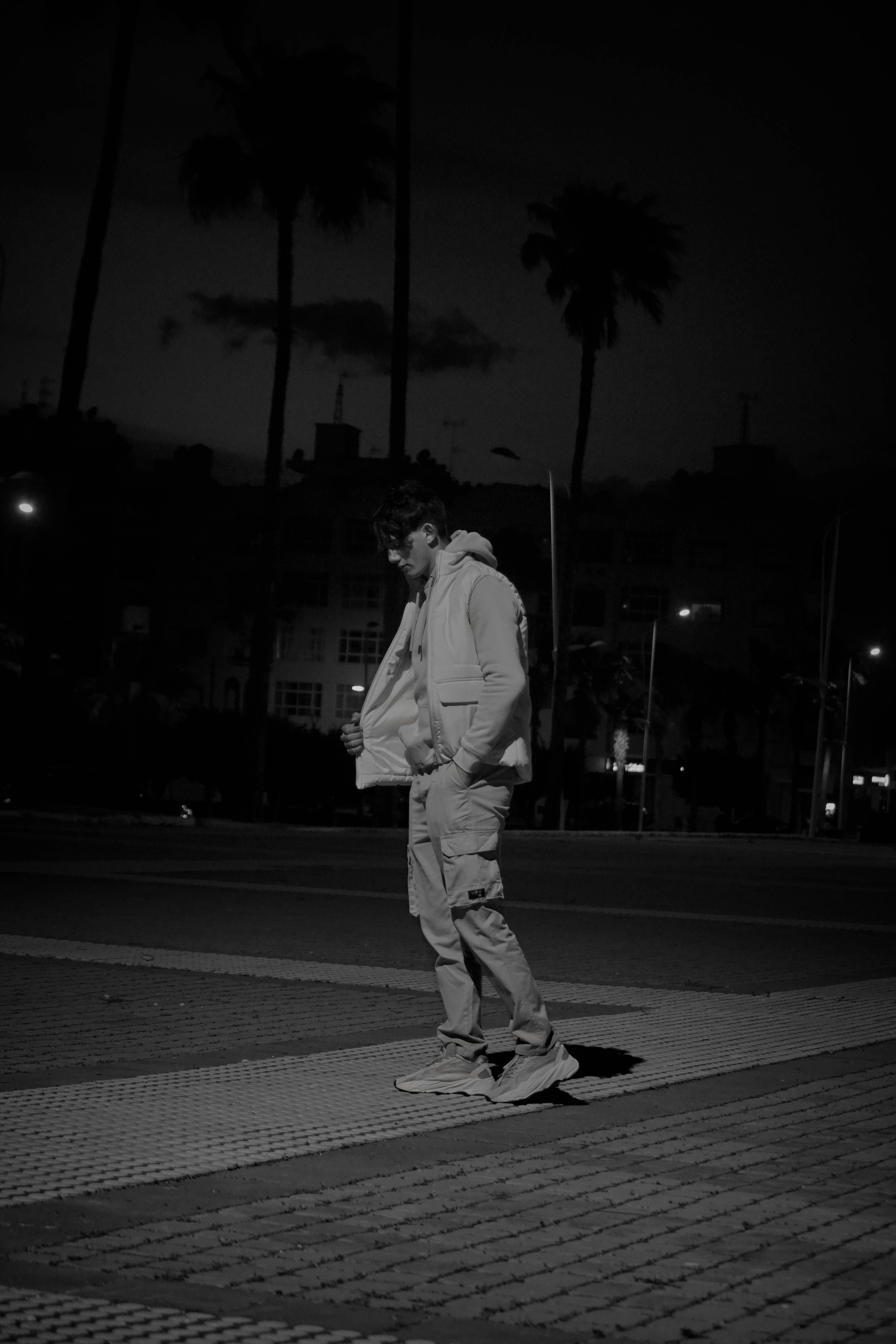 Stylish man in monochrome, posing on a city street at night in Tetouan, Morocco.