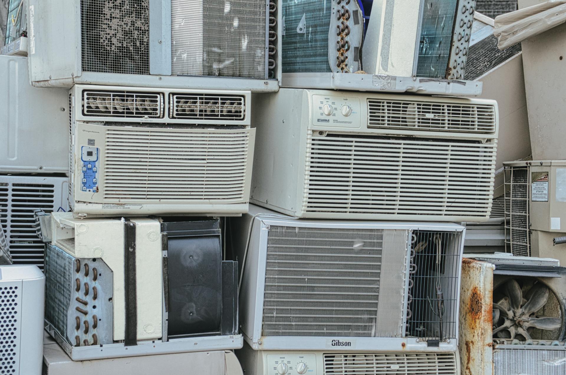 A pile of old window air conditioners awaits recycling, illustrating electronic waste issues.