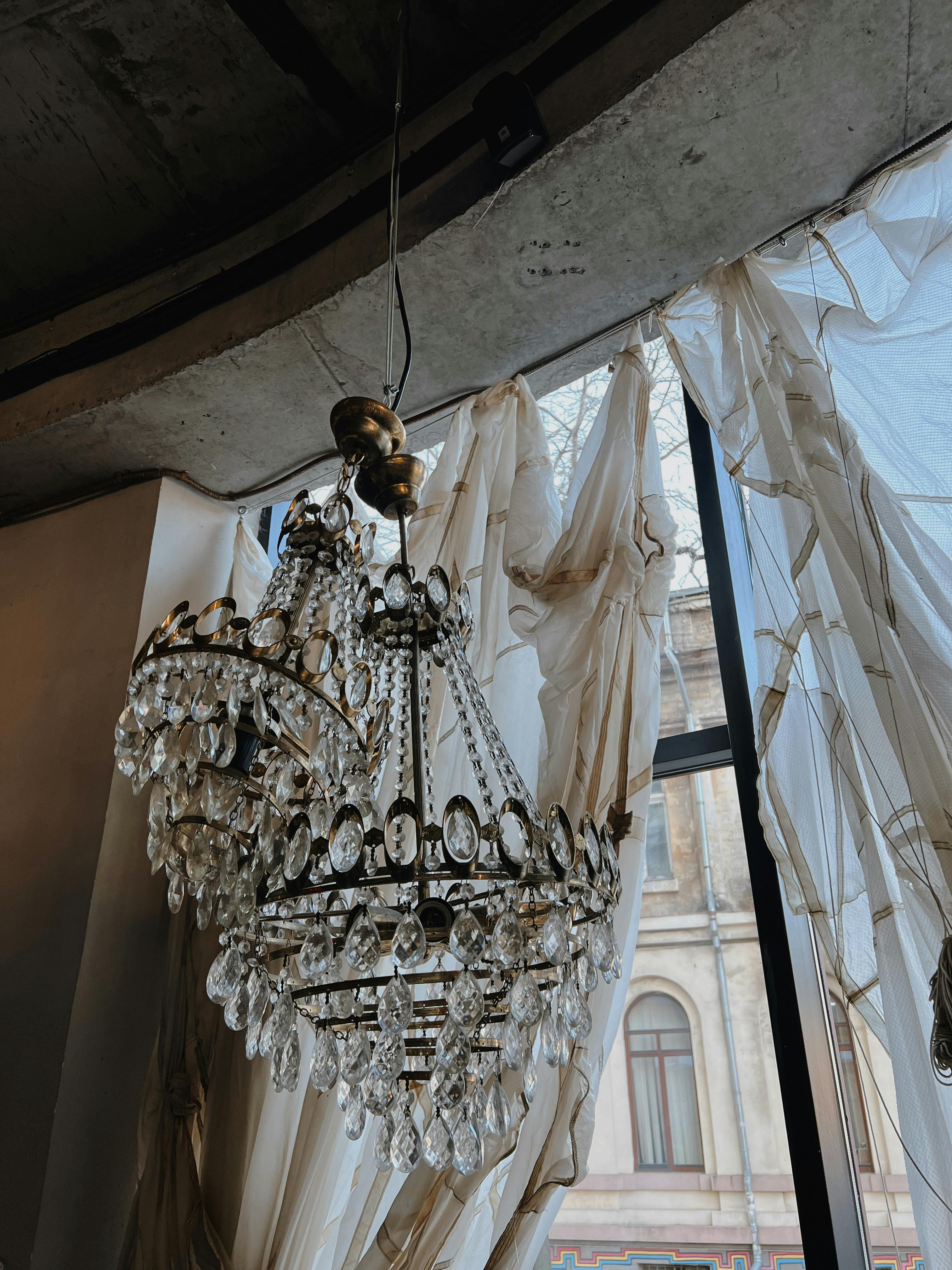 Crystal chandelier with draped curtains and architectural window view.