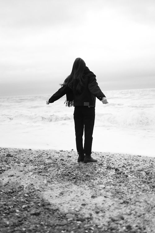 Free A black and white photo of a woman with arms outstretched, standing by the sea. Stock Photo
