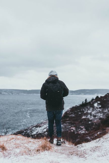 Person with backpack enjoying a snowy winter hike by the ocean.