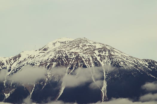 Majestic snow-capped mountain peak surrounded by clouds in Slovenia's serene landscape.