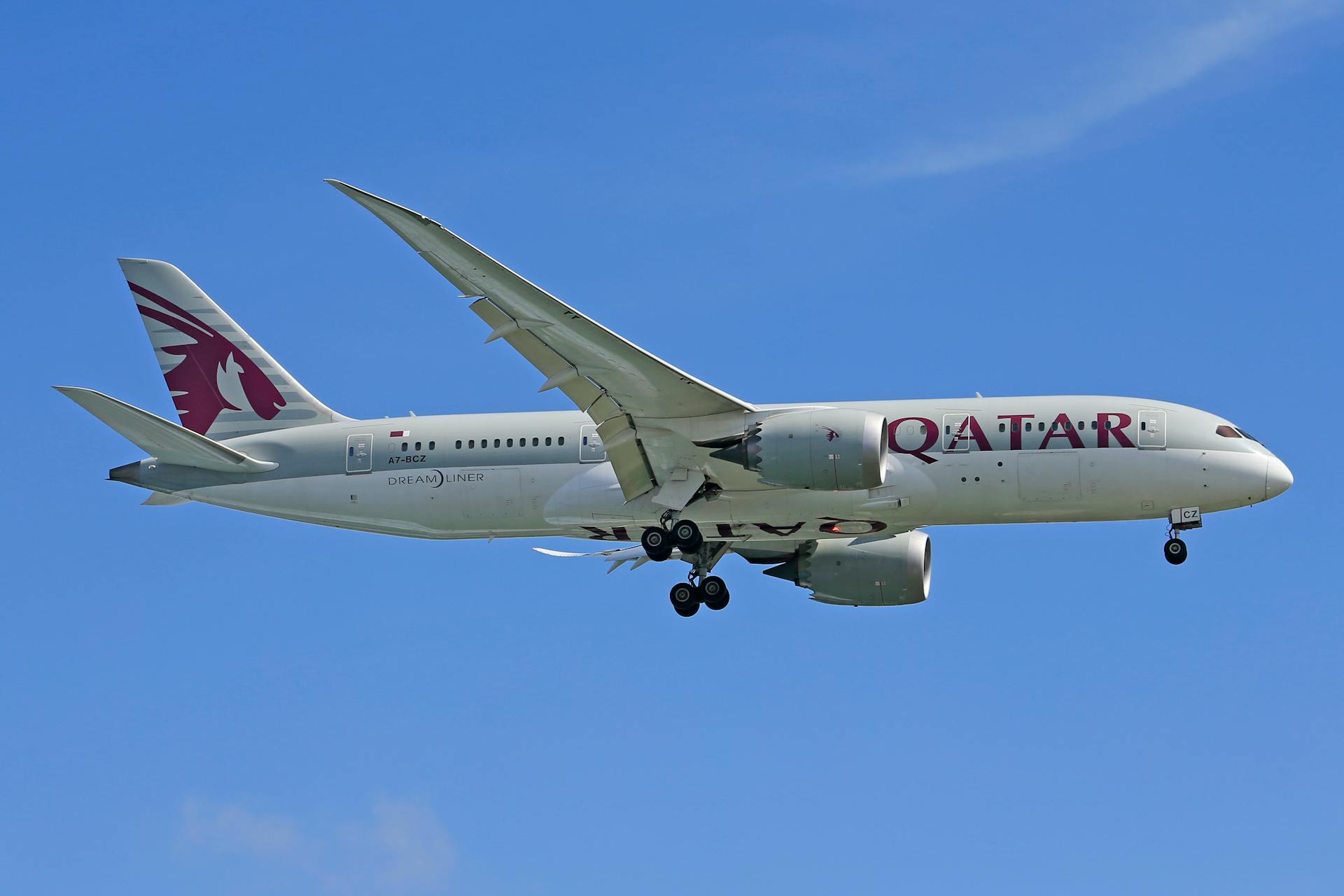 Qatar Airways Boeing 787 Dreamliner flying in clear blue sky.