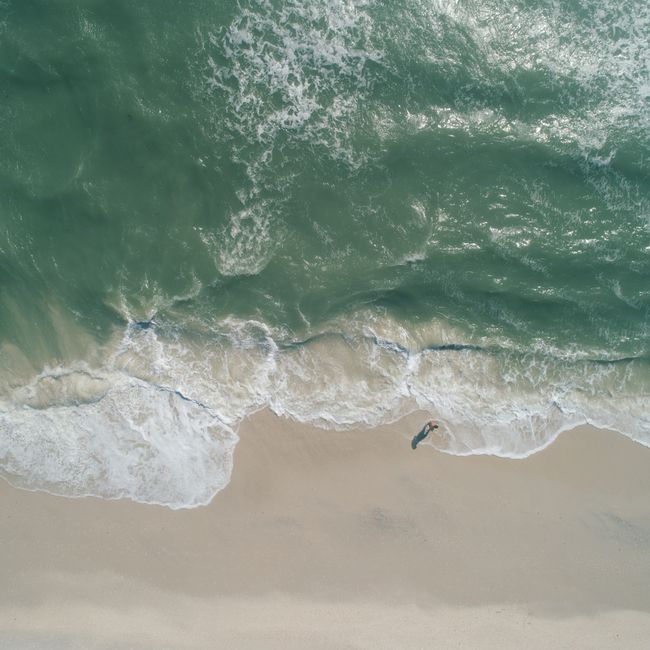 Top view of a tranquil beach with waves lapping the shore, a lone figure casts a shadow.