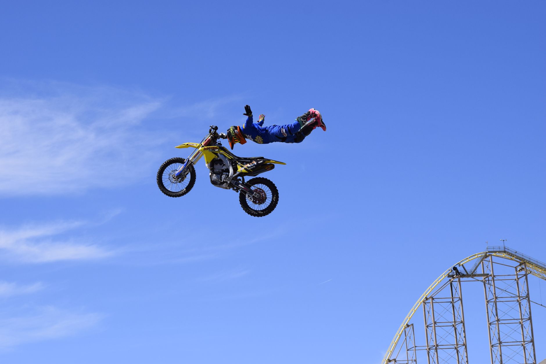 Motorcyclist performs an aerial stunt midair against a clear blue sky.