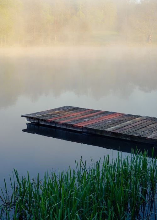 Free A tranquil foggy morning at a lake with a rustic wooden dock and surrounding nature. Stock Photo