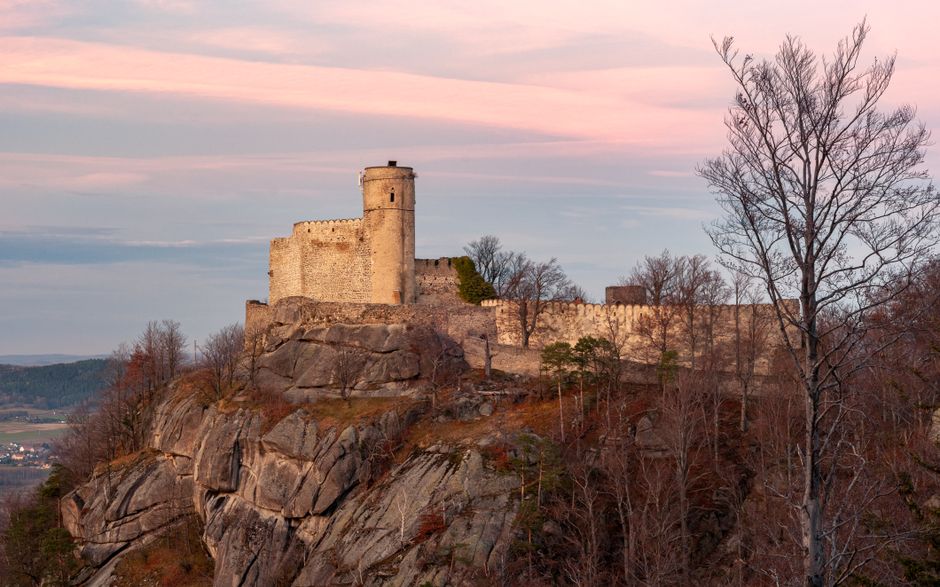 Středověký hrad na skalnatém ostrohu při západu slunce