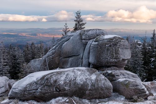 Free Scenic winter landscape with snow-covered boulders and coniferous trees under a cloudy sky. Stock Photo