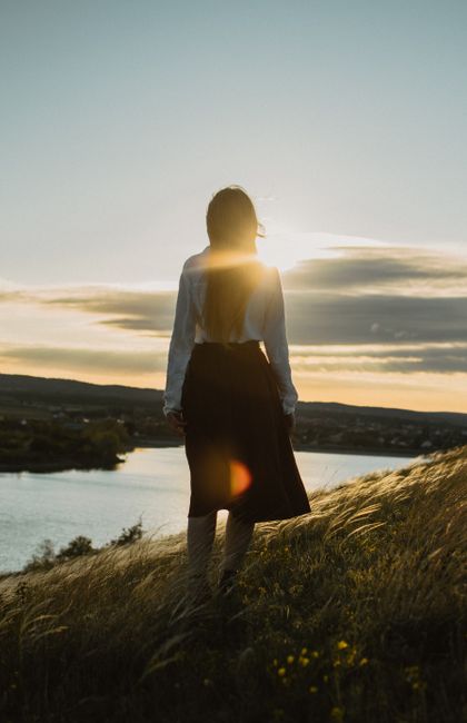 A woman stands on a hill at sunset, gazing over a tranquil river in Симферополь.