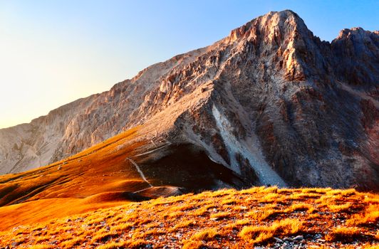 Vibrant landscape of the Gran Sasso mountains in Italy during sunrise, showcasing autumn colors.