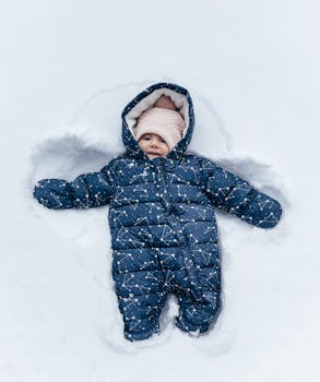 Cute baby in a snowsuit making a snow angel, enjoying winter outdoors.