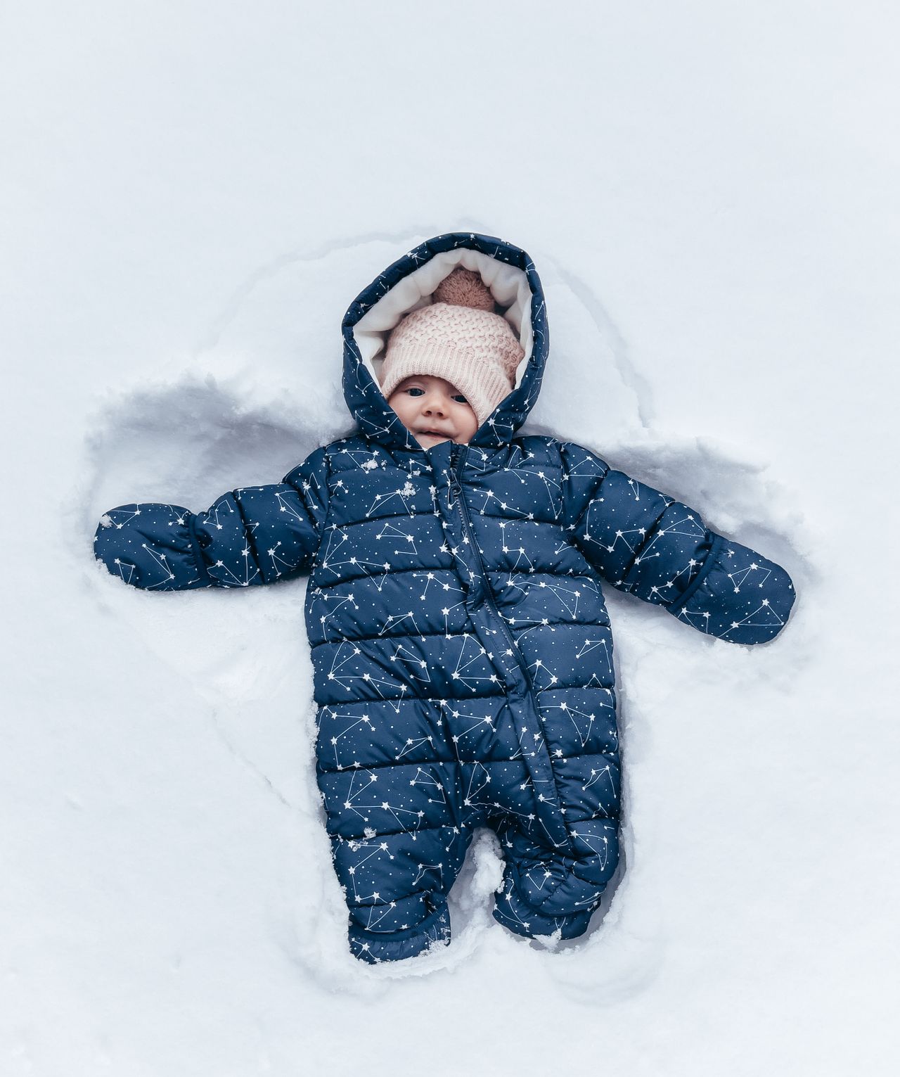 Baby in a navy snowsuit with hood making a snow angel