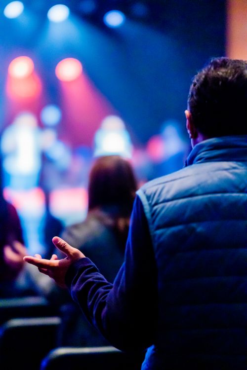 Free Audience at a worship concert, man praying, with vibrant stage lights. Stock Photo
