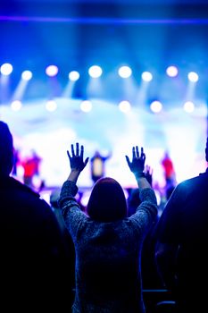 A woman raises her hands in praise during a vibrant indoor concert event.