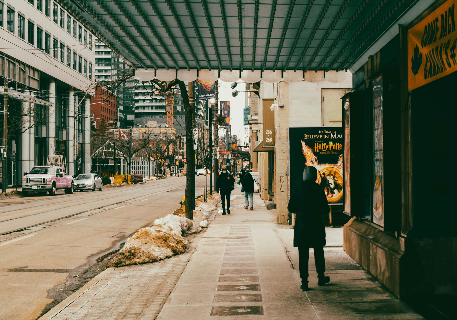 Urban winter scene in Toronto with people walking along a snowy sidewalk in the city.