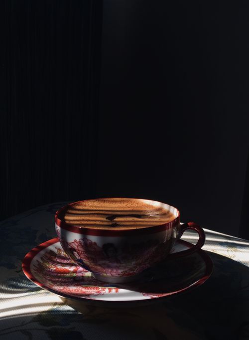 Free A beautifully crafted cup of coffee on a decorative saucer, bathed in warm, dramatic lighting. Stock Photo