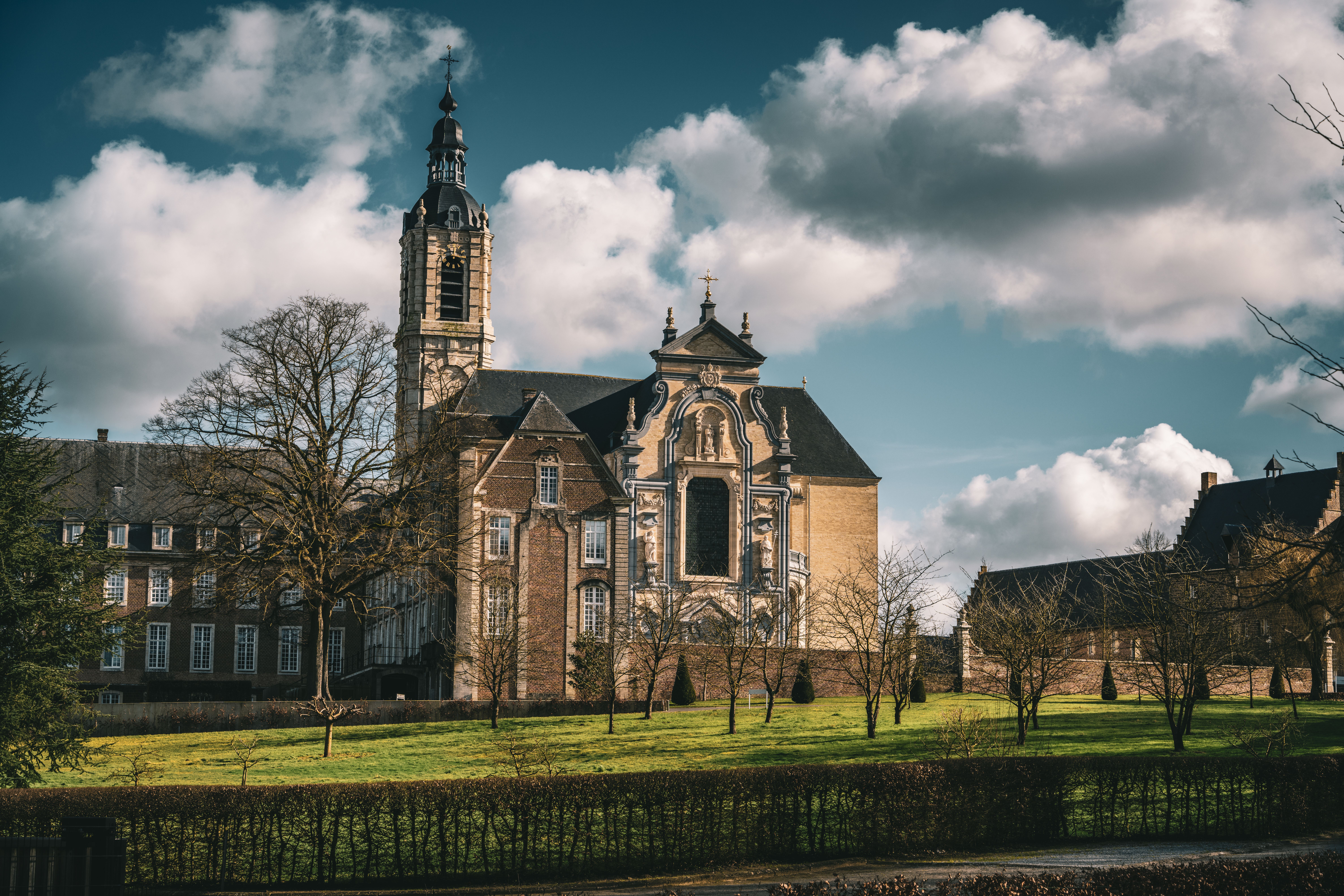 Beautiful abbey in Belgium with baroque architecture under a vibrant sky, surrounded by lush green fields.