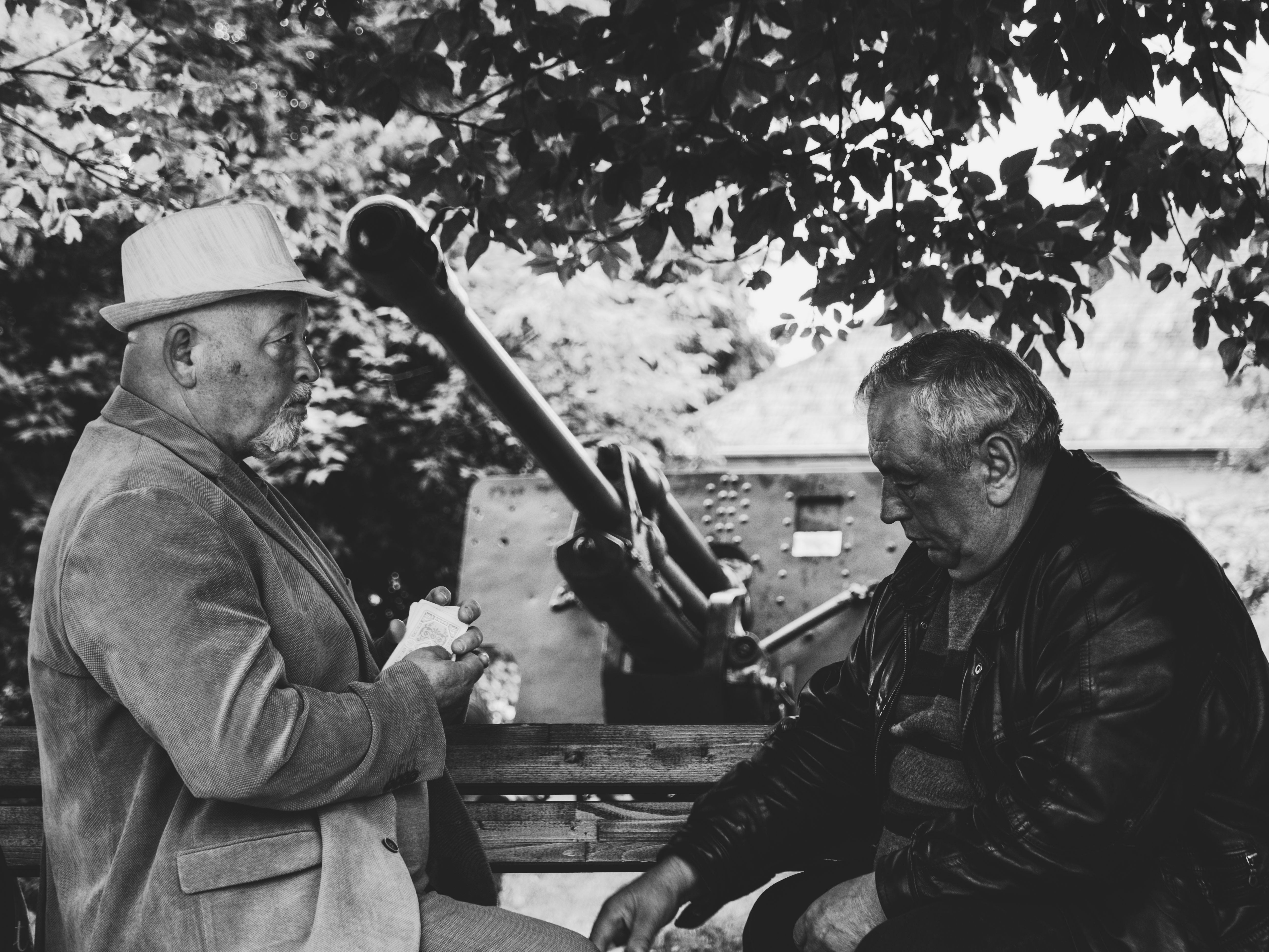 Two elderly men seated outdoors under a tree, deep in conversation, in a monochrome setting.