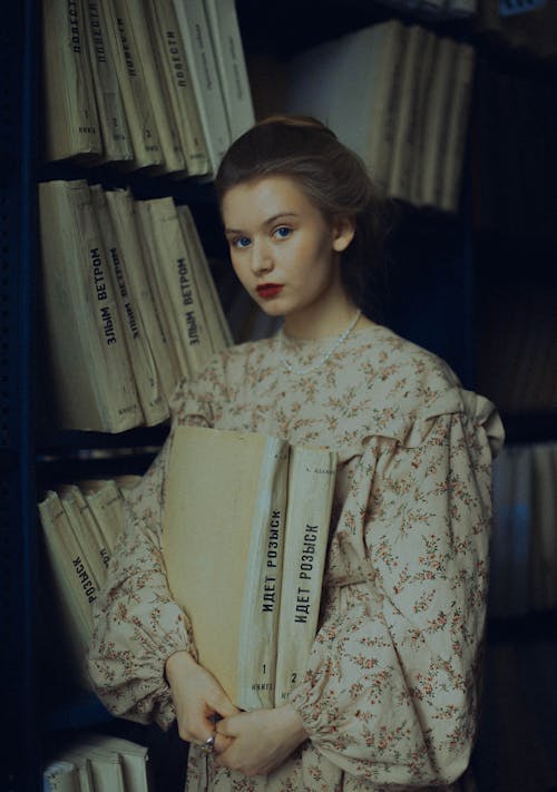 Free Girl in Old-fashioned Dress Standing in Library Holding Books  Stock Photo
