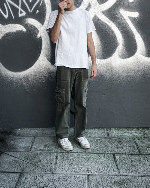 A Man in White Shirt and Gray Pants Standing Near the Concrete Wall