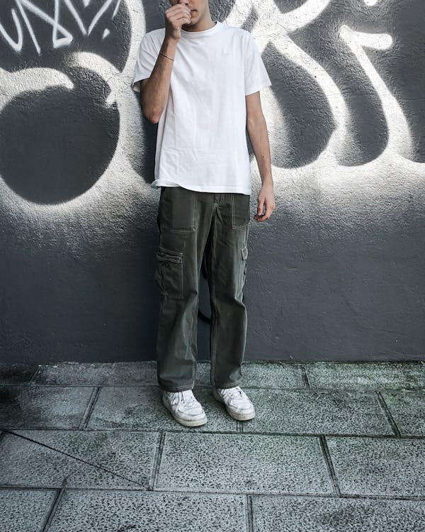 A Man in White Shirt and Gray Pants Standing Near the Concrete Wall