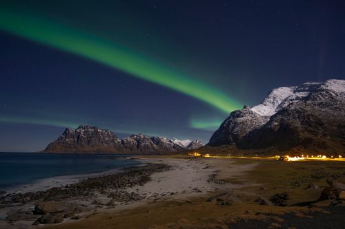 Free Breathtaking view of the Northern Lights dancing over snowy mountains on the Lofoten coastline in Norway. Stock Photo