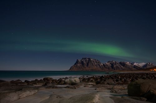 Free Stunning aurora borealis above the rocky shores and snowy mountains of Norway at night. Stock Photo