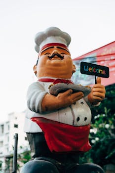 A cheerful chef statue holding a welcome sign, perfect for restaurants or food themes.