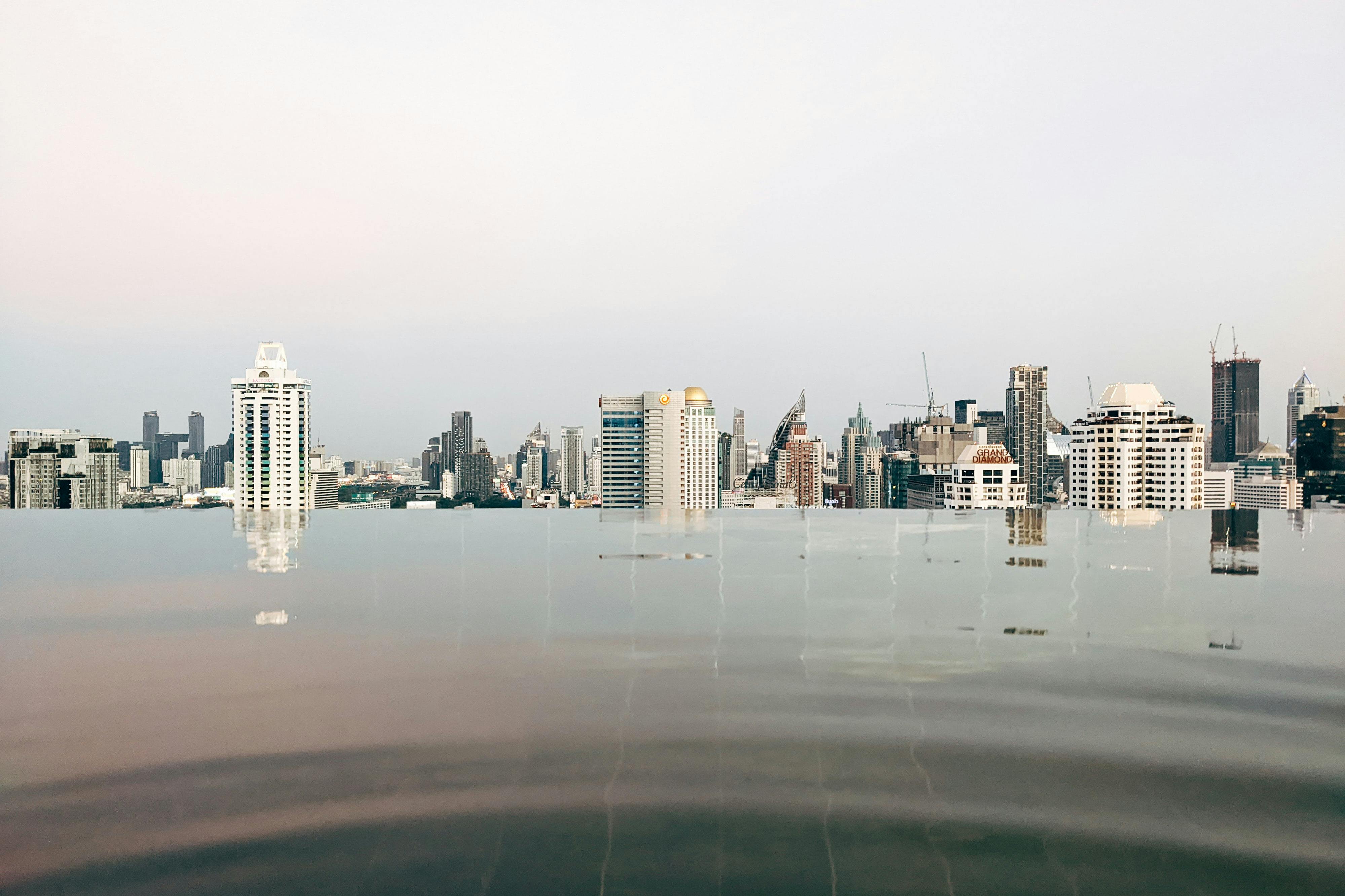 Tranquil infinity pool with reflections of the Bangkok skyline under a calm sky.