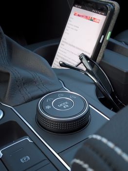 Detailed view of a car's drive mode selector knob and interior with a smartphone and glasses.