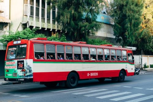 Free A red public bus driving along a city street with people inside and trees in the background. Stock Photo