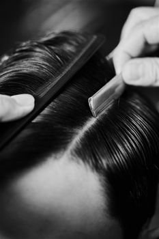 Black and white close-up of hair styling using a comb and razor in a barber shop.