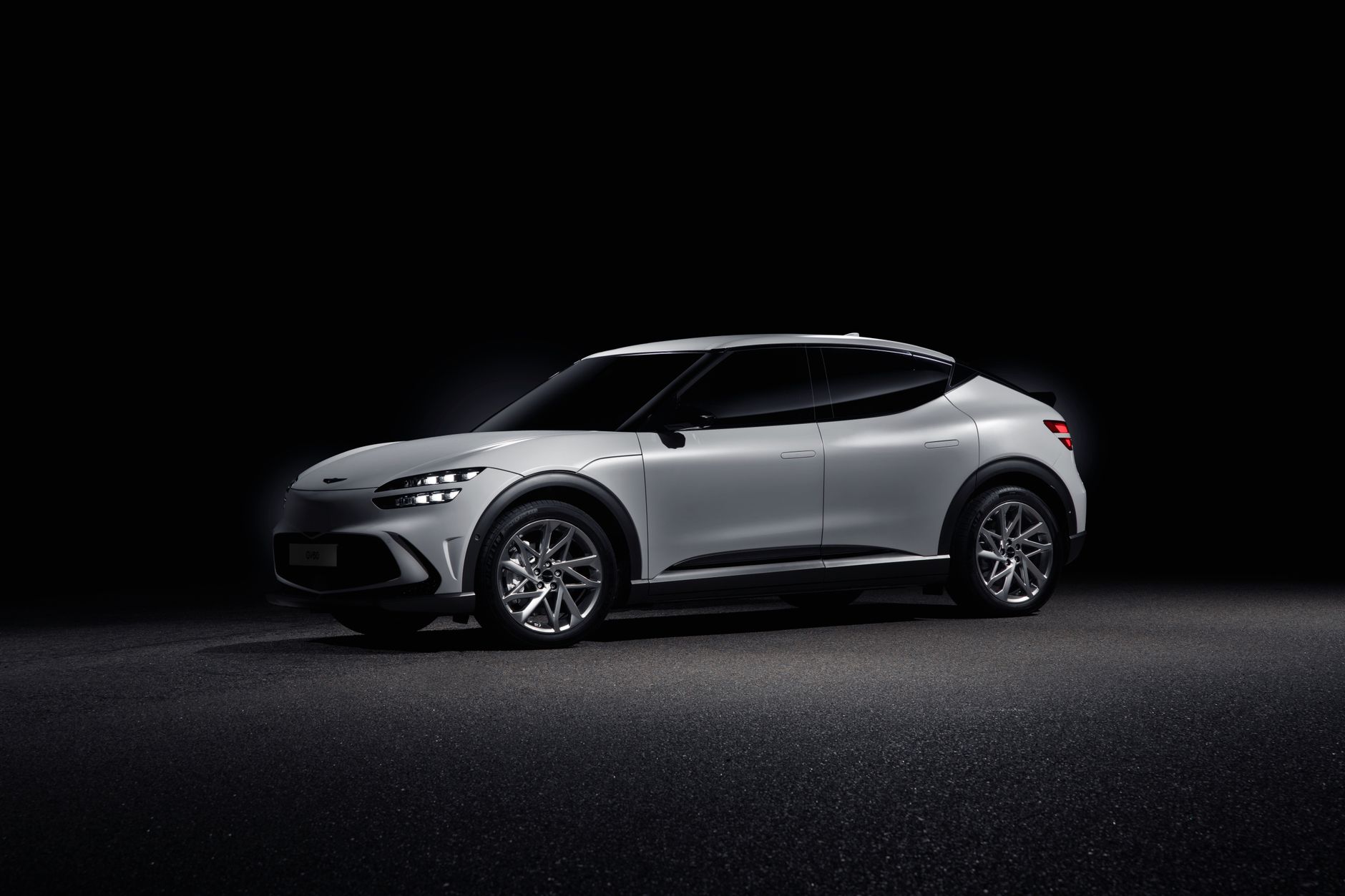 Sleek Genesis GV60 electric SUV in a studio with a black background, showcasing its elegant design.