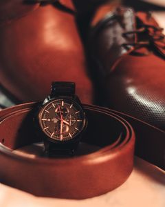 Close-up of a stylish men's wristwatch with leather shoes and belt, highlighting elegance and fashion.