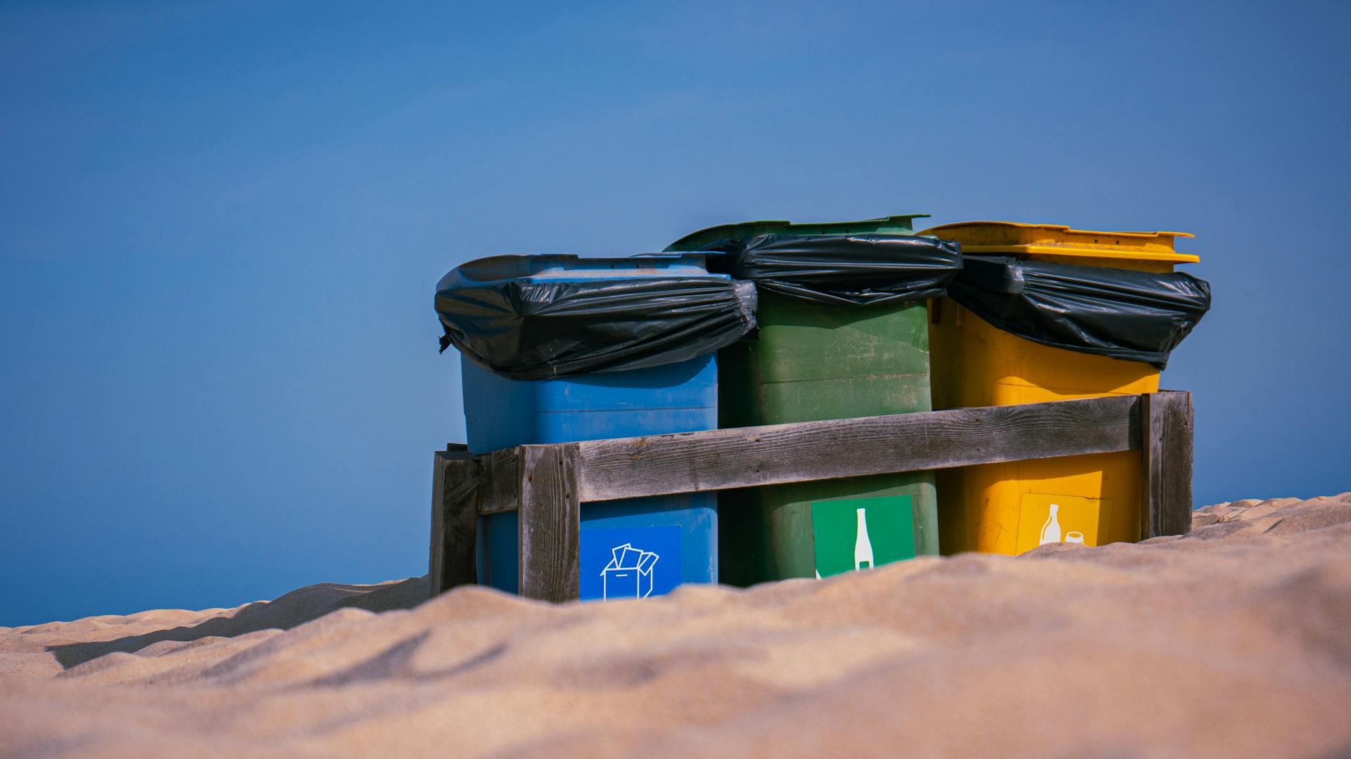 Colorful recycling bins for waste sorting on a sunny beach, promoting sustainability.