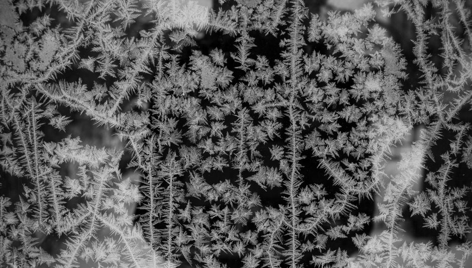 Close-up of intricate ice formations on a frosty window, creating a unique winter texture.