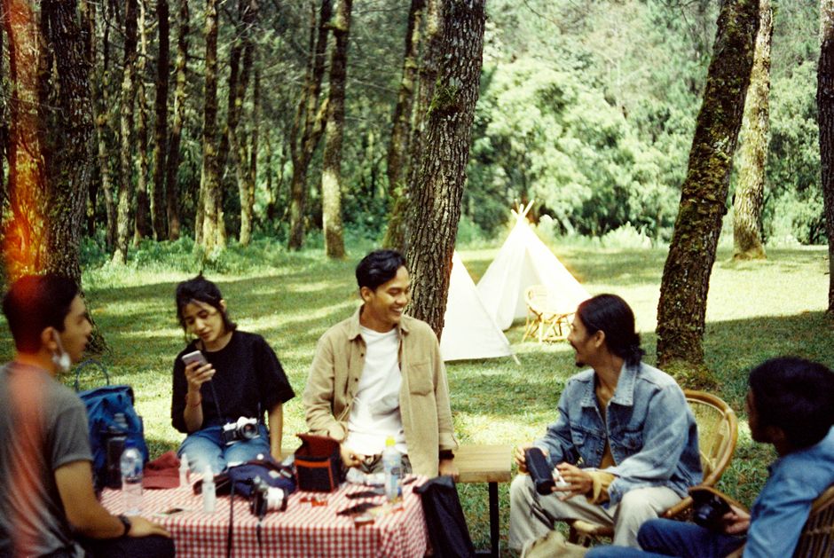 A group of friends enjoying a picnic in a forest with tents and nature around.