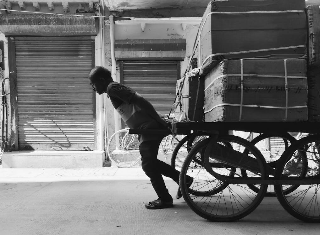 Grayscale Photo of a Man Pulling a Cart