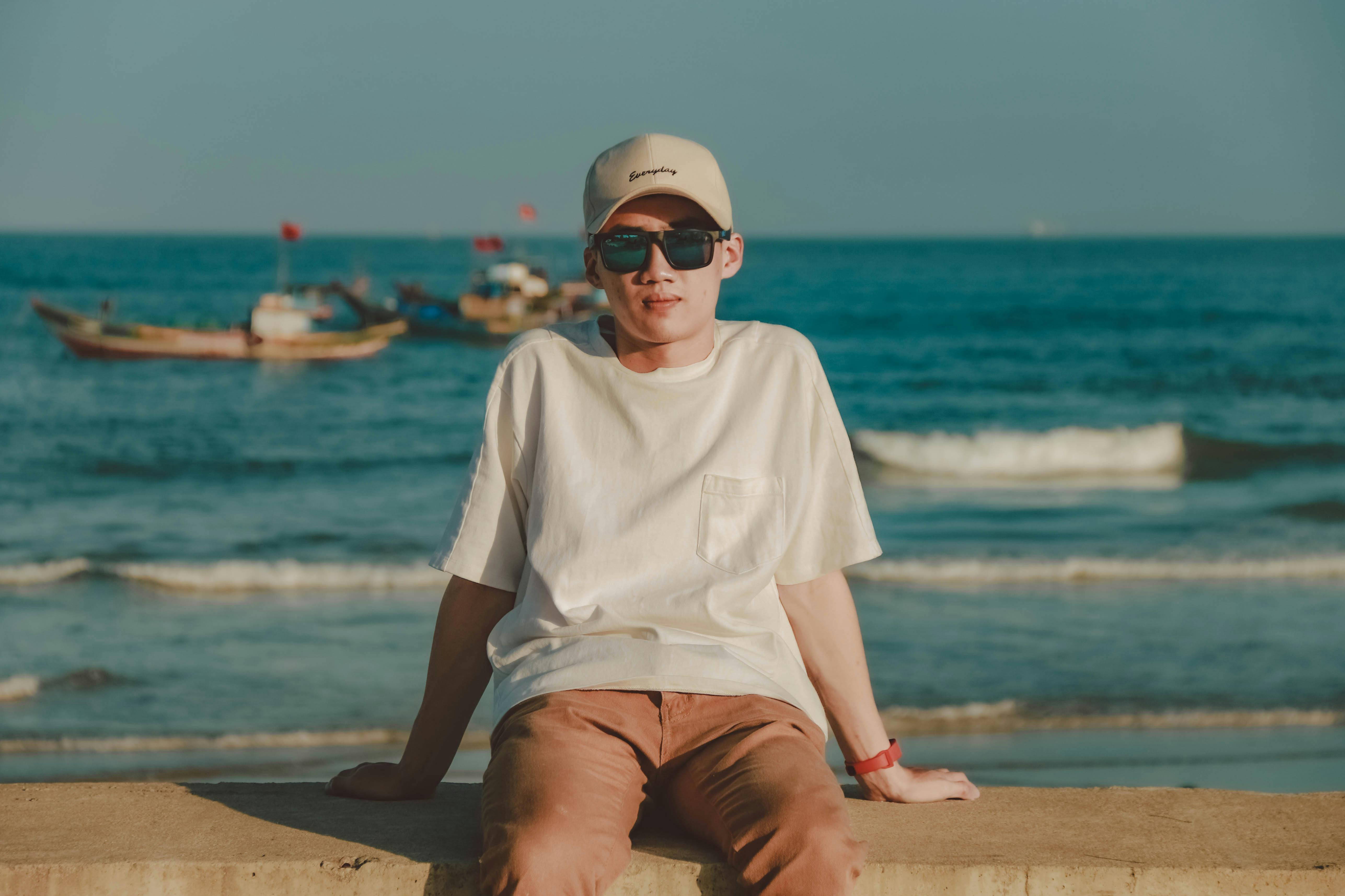 man in white crew neck t shirt and brown shorts sitting on brown sand near body