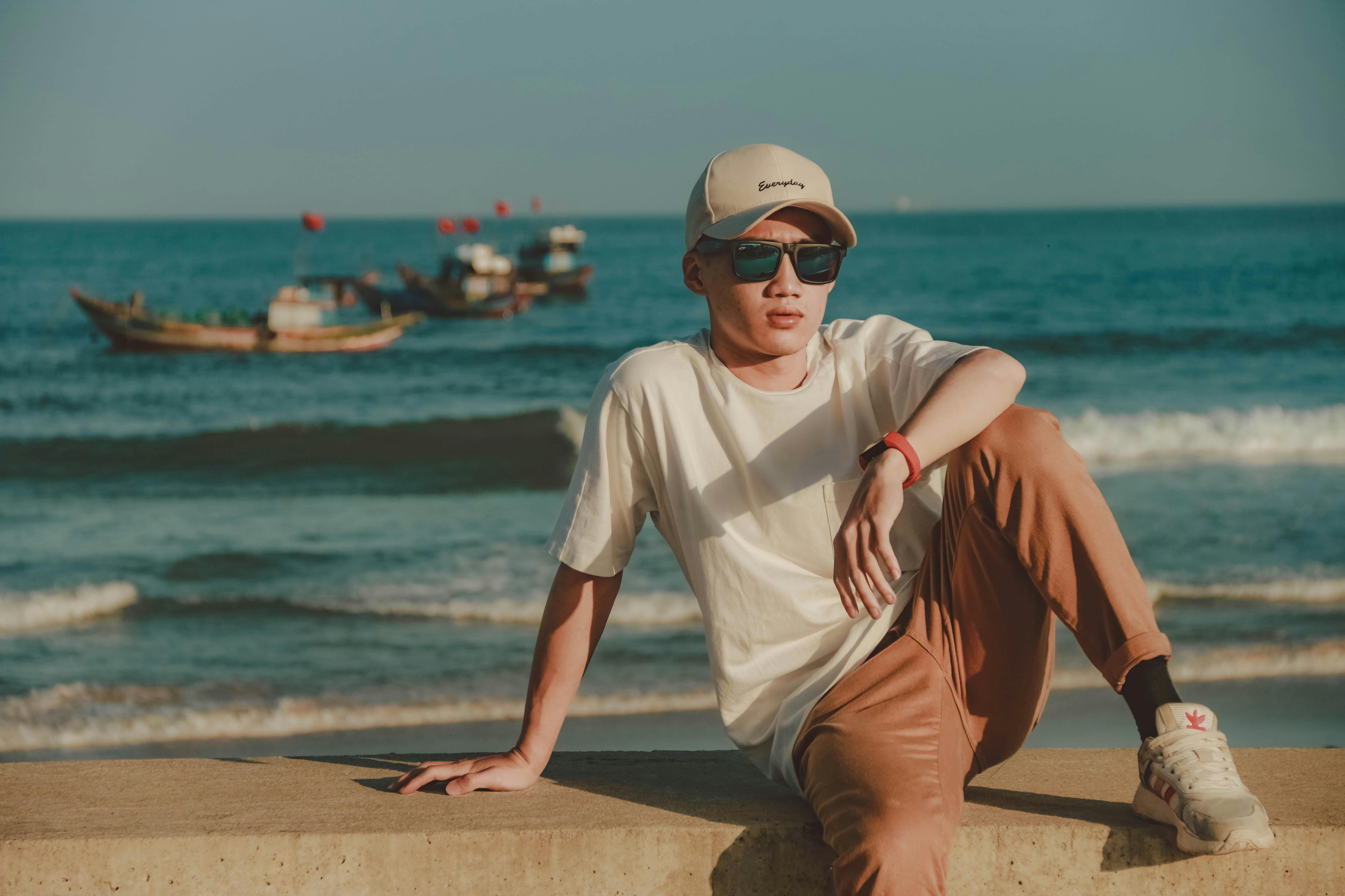 Free Man in White Crew Neck T-shirt and Brown Pants Sitting on Brown Concrete Dock during Stock Photo