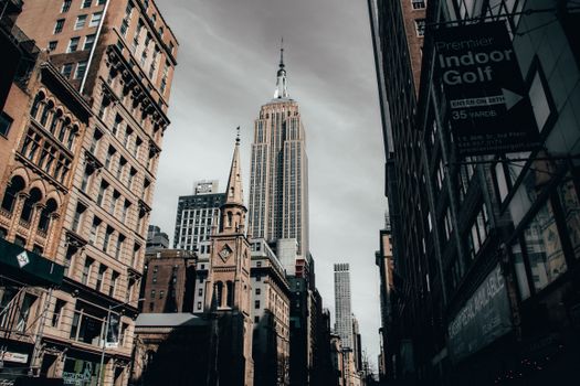 Low-angle view of Empire State Building surrounded by urban skyscrapers in New York City.