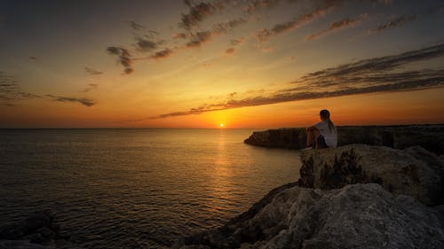 Kostenlos Foto Der Person, Die Auf Felsen Während Des Sonnenuntergangs Sitzt Stock-Foto