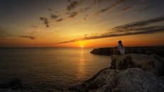 人坐在沿海悬崖看一个宁静的日落在海洋，创造一个和平和风景